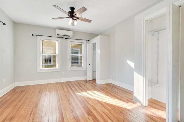 empty room featuring light wood-style flooring, baseboards, a ceiling fan, and a wall mounted AC