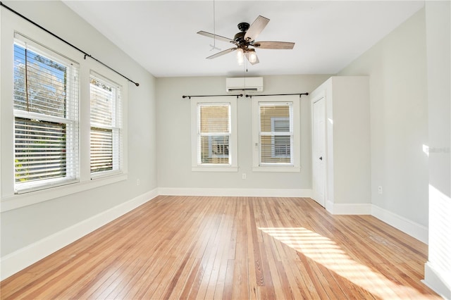 empty room with light wood-style floors, a wall mounted air conditioner, ceiling fan, and baseboards