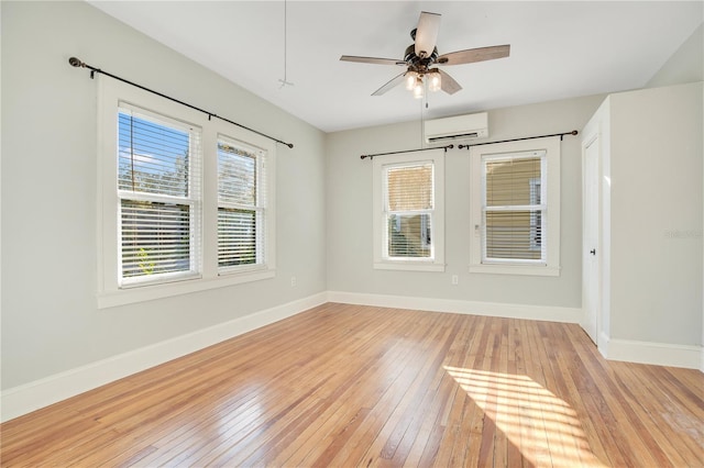 unfurnished room with ceiling fan, an AC wall unit, light wood-type flooring, and baseboards