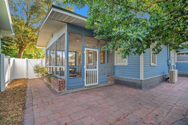 exterior space with cooling unit, a sunroom, fence, and a gate