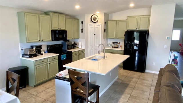 kitchen with sink, light tile patterned floors, black appliances, an island with sink, and green cabinetry