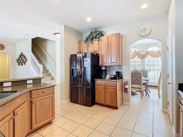 kitchen with dark stone countertops, black fridge with ice dispenser, decorative backsplash, and light tile patterned flooring