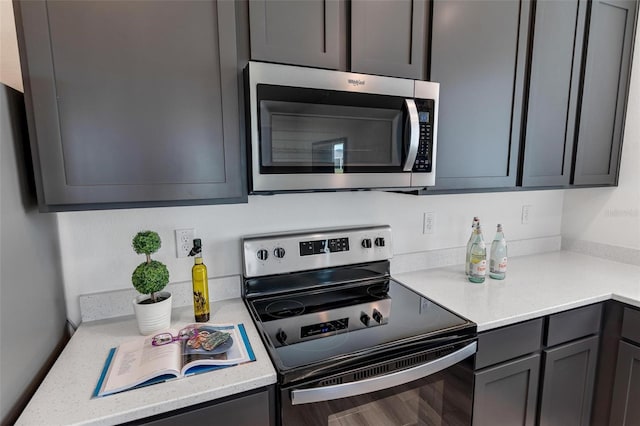 kitchen with stainless steel appliances, gray cabinets, and light stone countertops