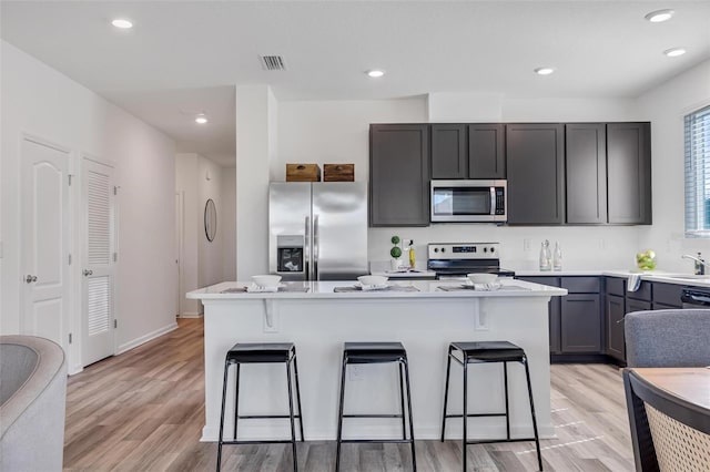 kitchen featuring a center island, light hardwood / wood-style flooring, appliances with stainless steel finishes, a kitchen breakfast bar, and light stone countertops