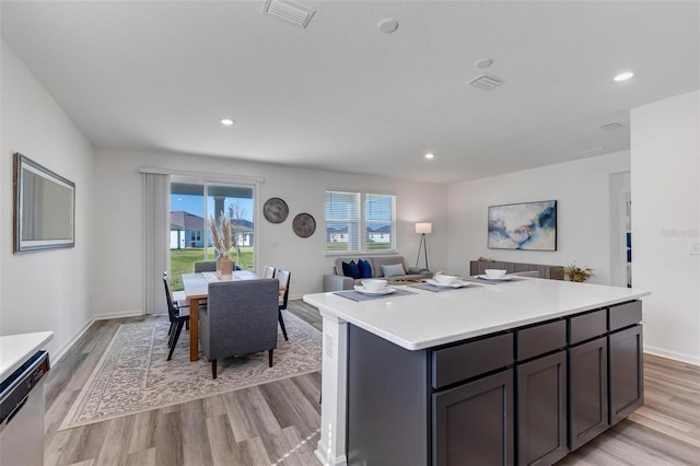 kitchen with a kitchen island, dark brown cabinets, stainless steel dishwasher, and light wood-type flooring