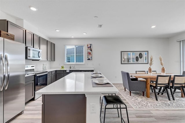 kitchen featuring a kitchen island, appliances with stainless steel finishes, a breakfast bar area, and light hardwood / wood-style floors