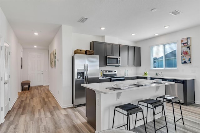 kitchen with a breakfast bar area, a center island, a textured ceiling, light hardwood / wood-style flooring, and appliances with stainless steel finishes