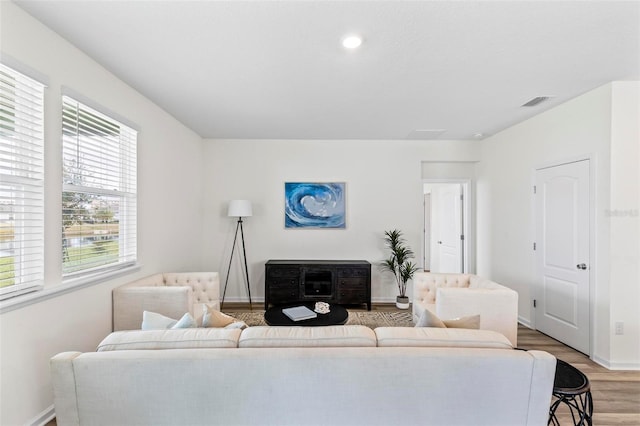 living room with light wood-type flooring, visible vents, and baseboards