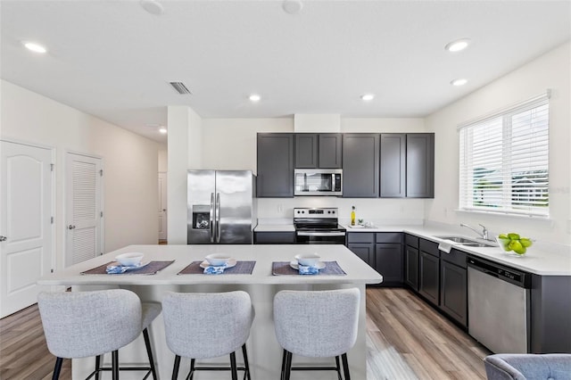 kitchen with stainless steel appliances, light countertops, light wood-style floors, a sink, and a kitchen island