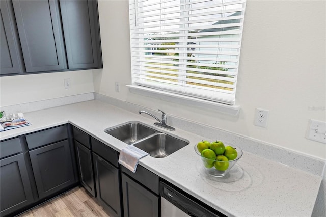 kitchen featuring a sink, light wood finished floors, dishwasher, and light stone countertops