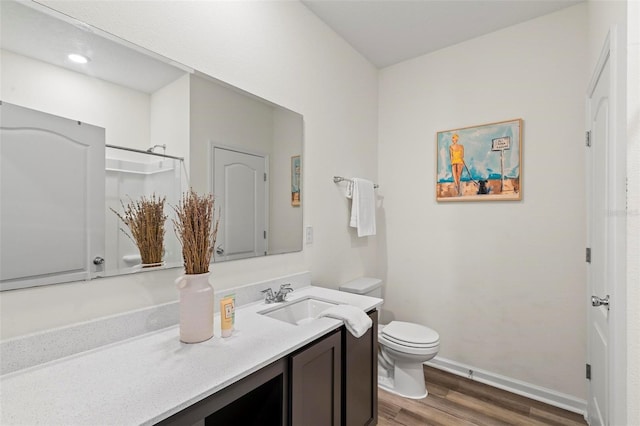 bathroom with toilet, wood finished floors, vanity, baseboards, and walk in shower