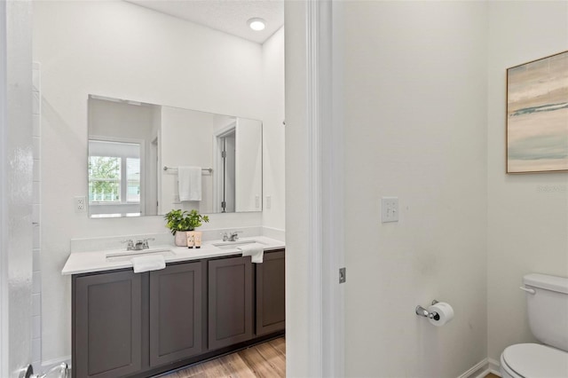 full bath with double vanity, toilet, a sink, wood finished floors, and baseboards