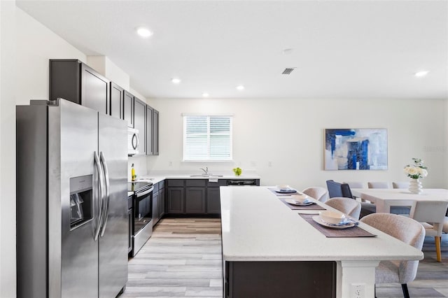 kitchen featuring light wood-style flooring, appliances with stainless steel finishes, light stone counters, a center island, and a sink