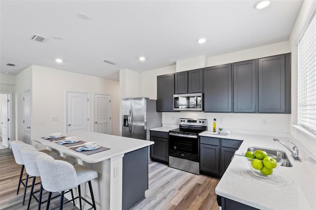 kitchen with a center island, stainless steel appliances, light wood-style floors, a kitchen bar, and a sink