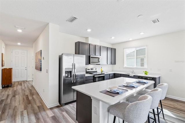 kitchen featuring a breakfast bar area, stainless steel appliances, a kitchen island, visible vents, and light countertops