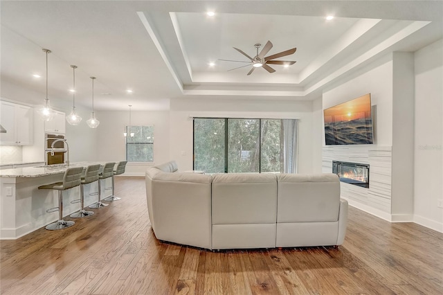 living room featuring sink, light hardwood / wood-style flooring, ceiling fan, and a tray ceiling