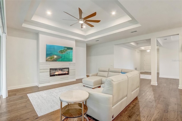 living room featuring ceiling fan, a raised ceiling, and light wood-type flooring