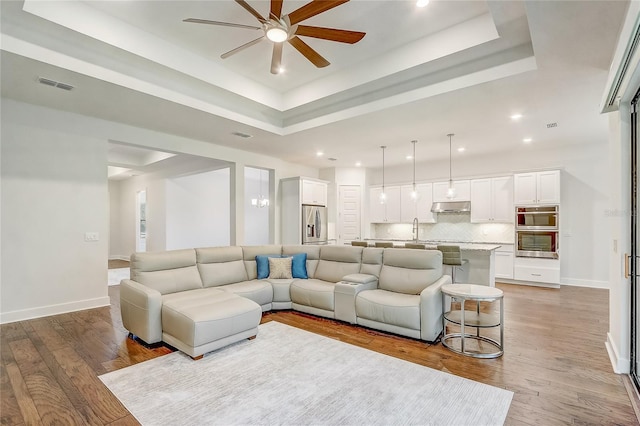 living room with hardwood / wood-style flooring, ceiling fan, a raised ceiling, and sink