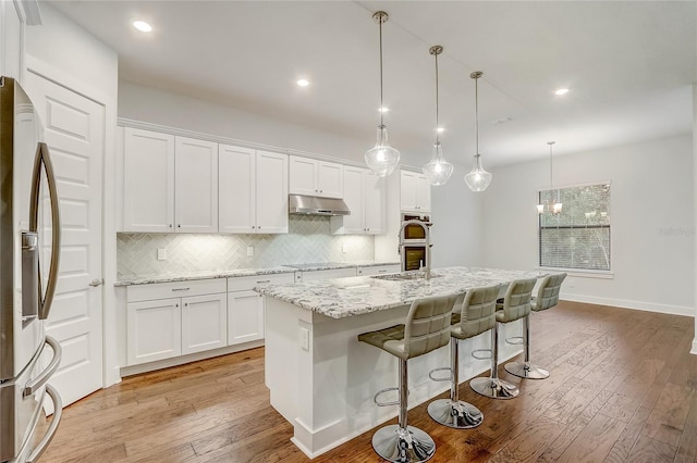 kitchen featuring pendant lighting, appliances with stainless steel finishes, white cabinets, and a center island with sink