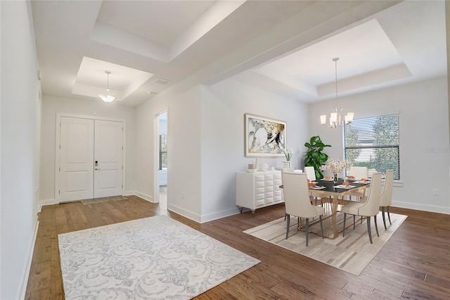 dining area featuring dark hardwood / wood-style flooring, a tray ceiling, and an inviting chandelier