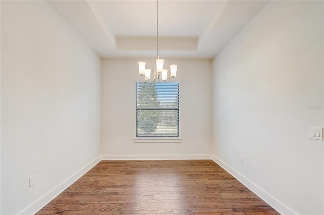 spare room featuring a raised ceiling, hardwood / wood-style floors, and an inviting chandelier