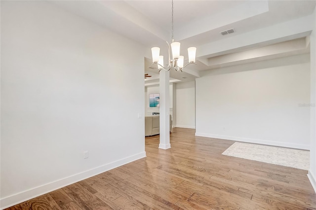 unfurnished dining area with hardwood / wood-style floors, a chandelier, and a tray ceiling