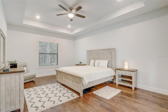 bedroom with light hardwood / wood-style flooring, ceiling fan, and a tray ceiling