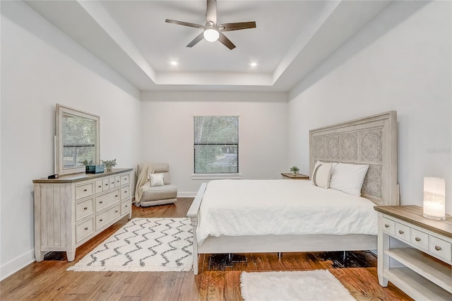 bedroom featuring a tray ceiling, ceiling fan, and light hardwood / wood-style flooring