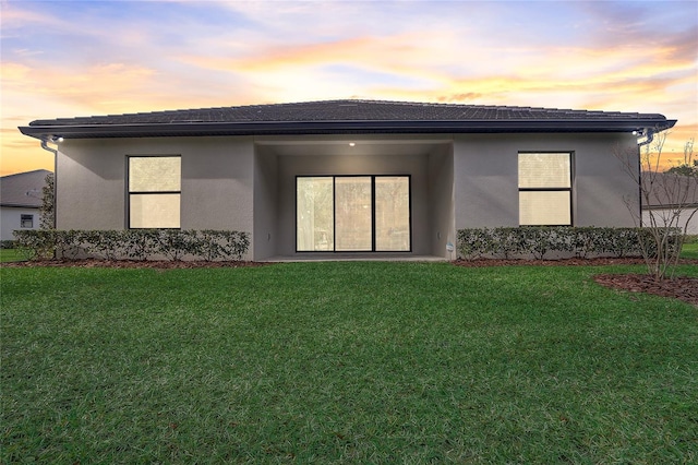 back house at dusk featuring a lawn