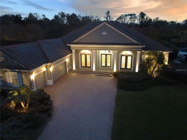 view of front of house with decorative driveway, french doors, stucco siding, an attached garage, and a tiled roof