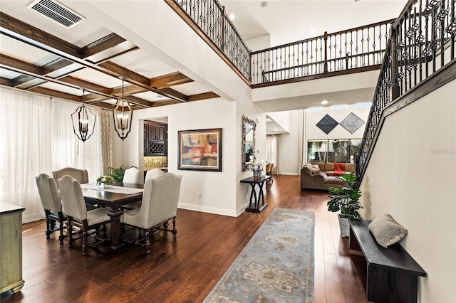 dining space featuring dark hardwood / wood-style floors, a towering ceiling, beamed ceiling, coffered ceiling, and a notable chandelier