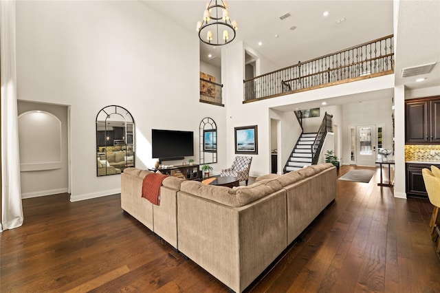 living room featuring dark wood-type flooring, a towering ceiling, and an inviting chandelier