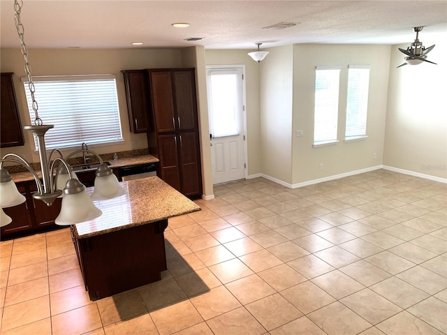 kitchen featuring a center island, hanging light fixtures, dark brown cabinets, a healthy amount of sunlight, and light stone countertops