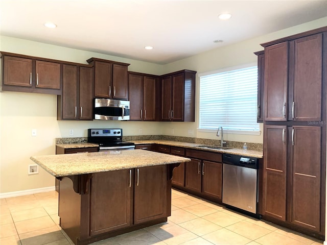 kitchen with a kitchen bar, sink, a center island, appliances with stainless steel finishes, and light stone countertops