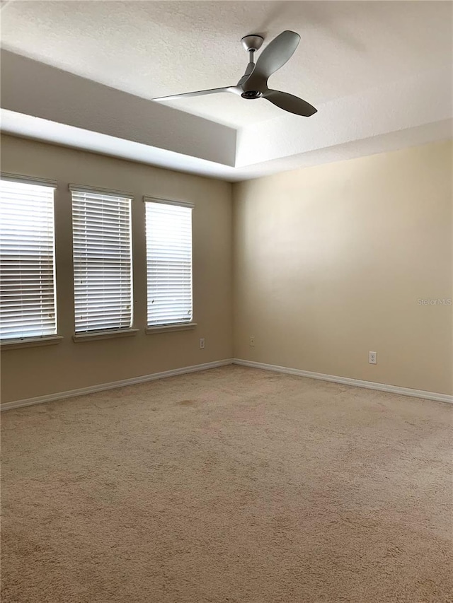 carpeted empty room with a textured ceiling, ceiling fan, and a tray ceiling