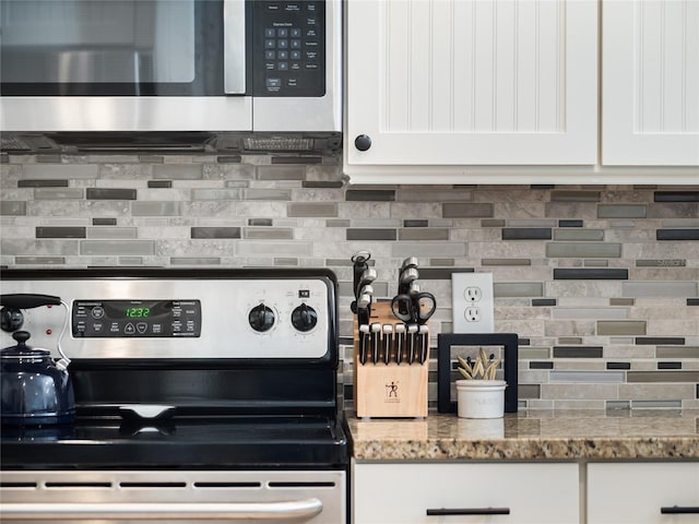 kitchen featuring appliances with stainless steel finishes, dark stone countertops, white cabinets, and backsplash