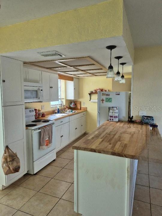 kitchen with sink, white cabinetry, decorative light fixtures, light tile patterned floors, and white appliances