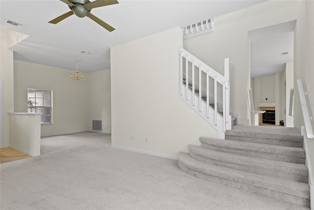 stairs with carpet and ceiling fan with notable chandelier