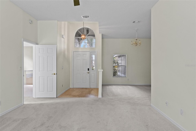 entrance foyer with an inviting chandelier, light colored carpet, a textured ceiling, and a high ceiling