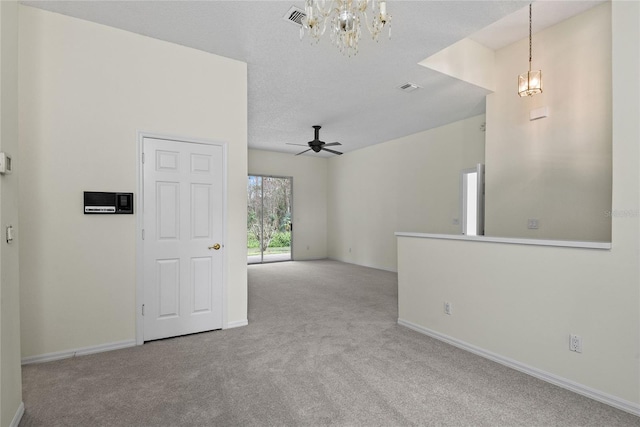 empty room featuring light carpet, ceiling fan with notable chandelier, and a textured ceiling