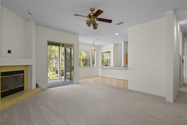 unfurnished living room featuring a tile fireplace, ceiling fan with notable chandelier, light carpet, and a textured ceiling