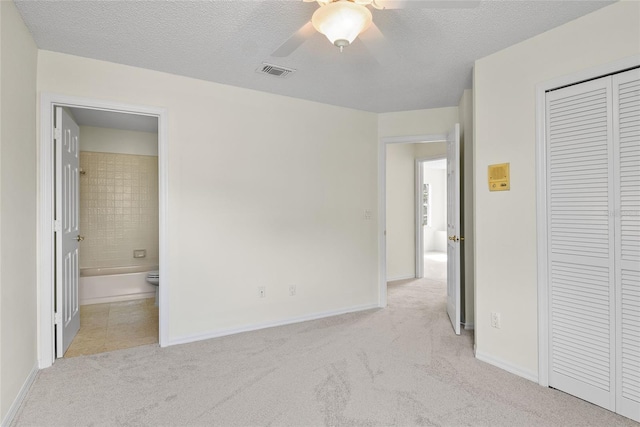 unfurnished bedroom featuring ensuite bathroom, light colored carpet, ceiling fan, a textured ceiling, and a closet