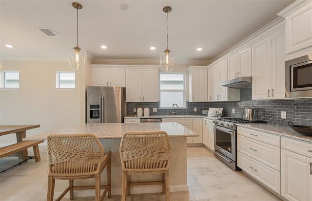 kitchen with high quality appliances, sink, hanging light fixtures, a center island, and light stone countertops