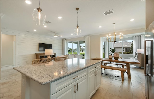 kitchen with light stone counters, a center island, hanging light fixtures, and white cabinets