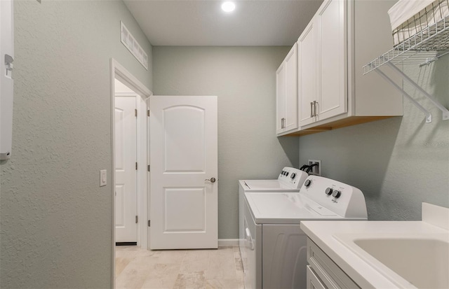 clothes washing area with sink, washing machine and dryer, and cabinets