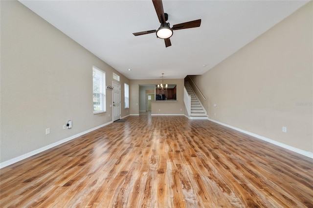 unfurnished living room with ceiling fan with notable chandelier and light hardwood / wood-style flooring