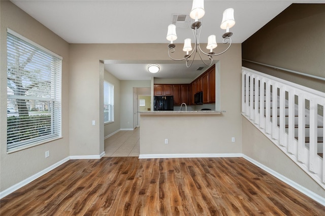 kitchen with sink, light hardwood / wood-style flooring, kitchen peninsula, a notable chandelier, and black appliances