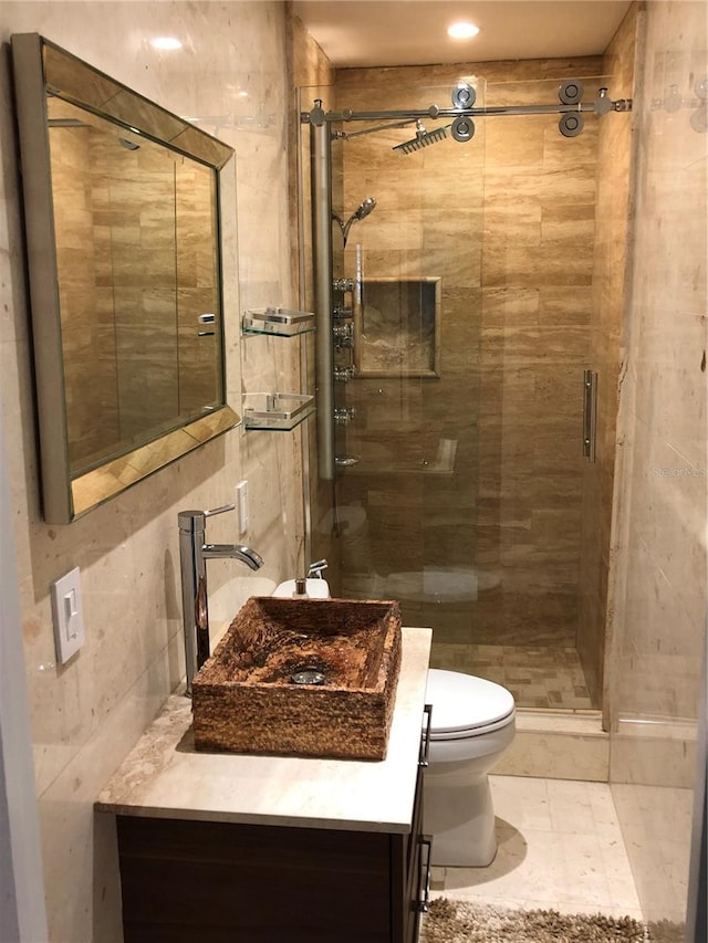 bathroom featuring vanity, toilet, tile walls, and a shower with shower door