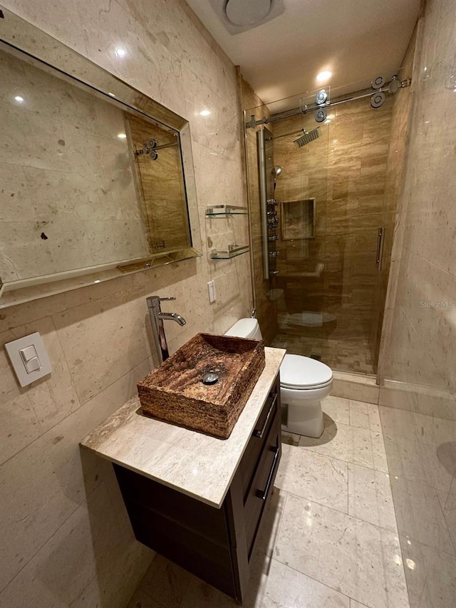 bathroom with vanity, toilet, a shower with door, and tile walls