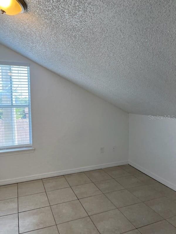 bonus room with lofted ceiling, tile patterned floors, and a textured ceiling